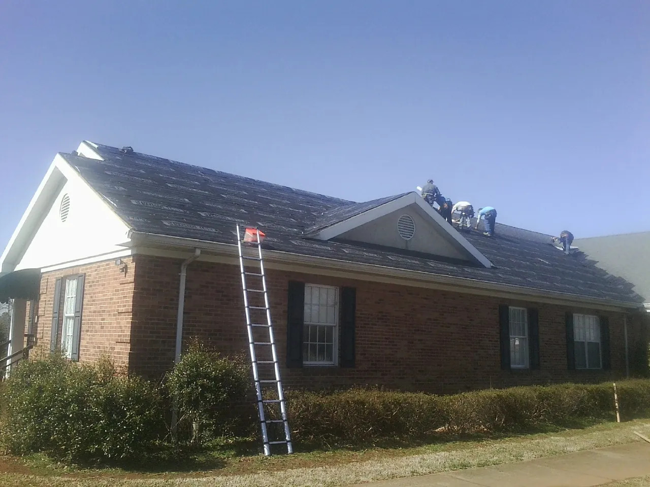 Crew tearing shingles off a brick ranch roof with a ladder set — Metal Roof Repair work by our crew in Kendallville