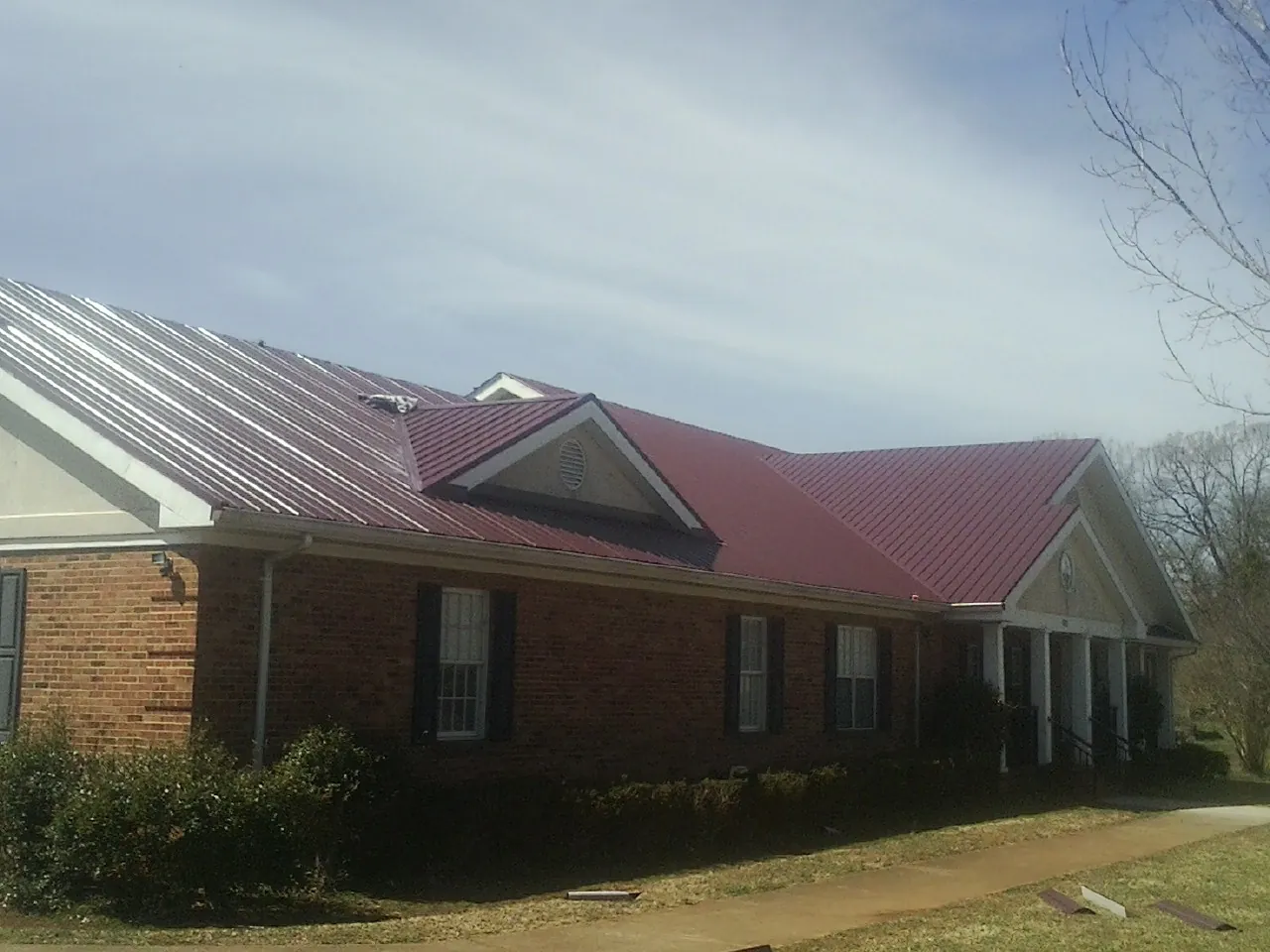 Red metal roof with gabled entries on a long brick building, from a Hail Damage Roof Repair job in Kendallville