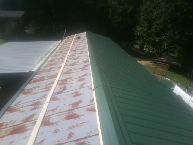 Old rusted panels beside newly installed green metal roofing — Wind Damage Roof Repair by Roofing Brothers in Kendallville