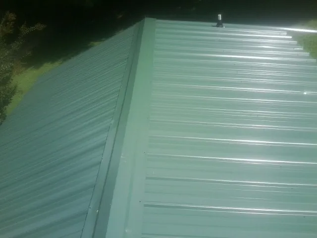 New green metal panels meeting at the ridge of a roof — Flat Roof Repair work by our crew in Kendallville