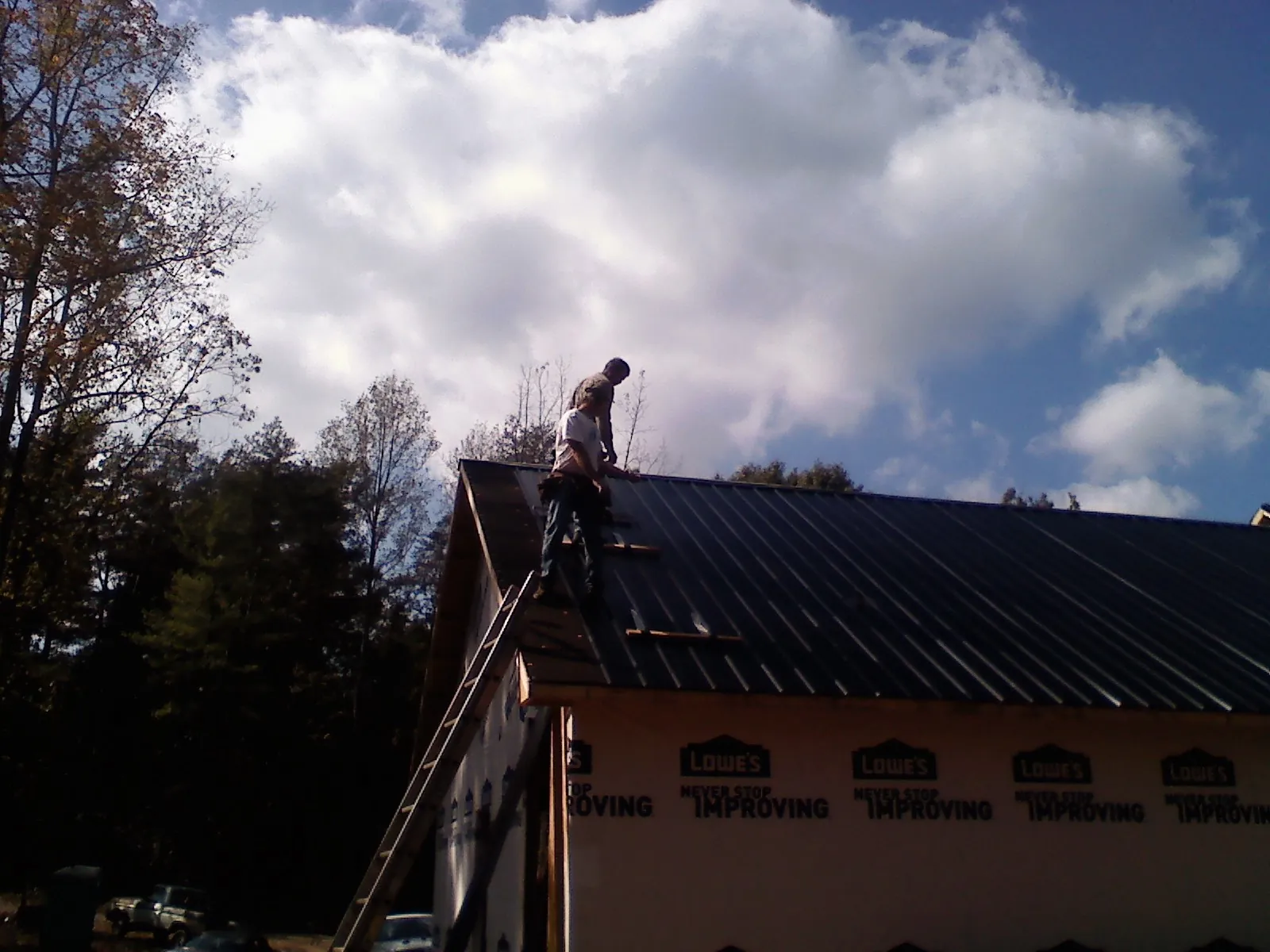 Roofer fastening dark metal panels high against a cloudy sky, from a Roof Inspection job in Kendallville