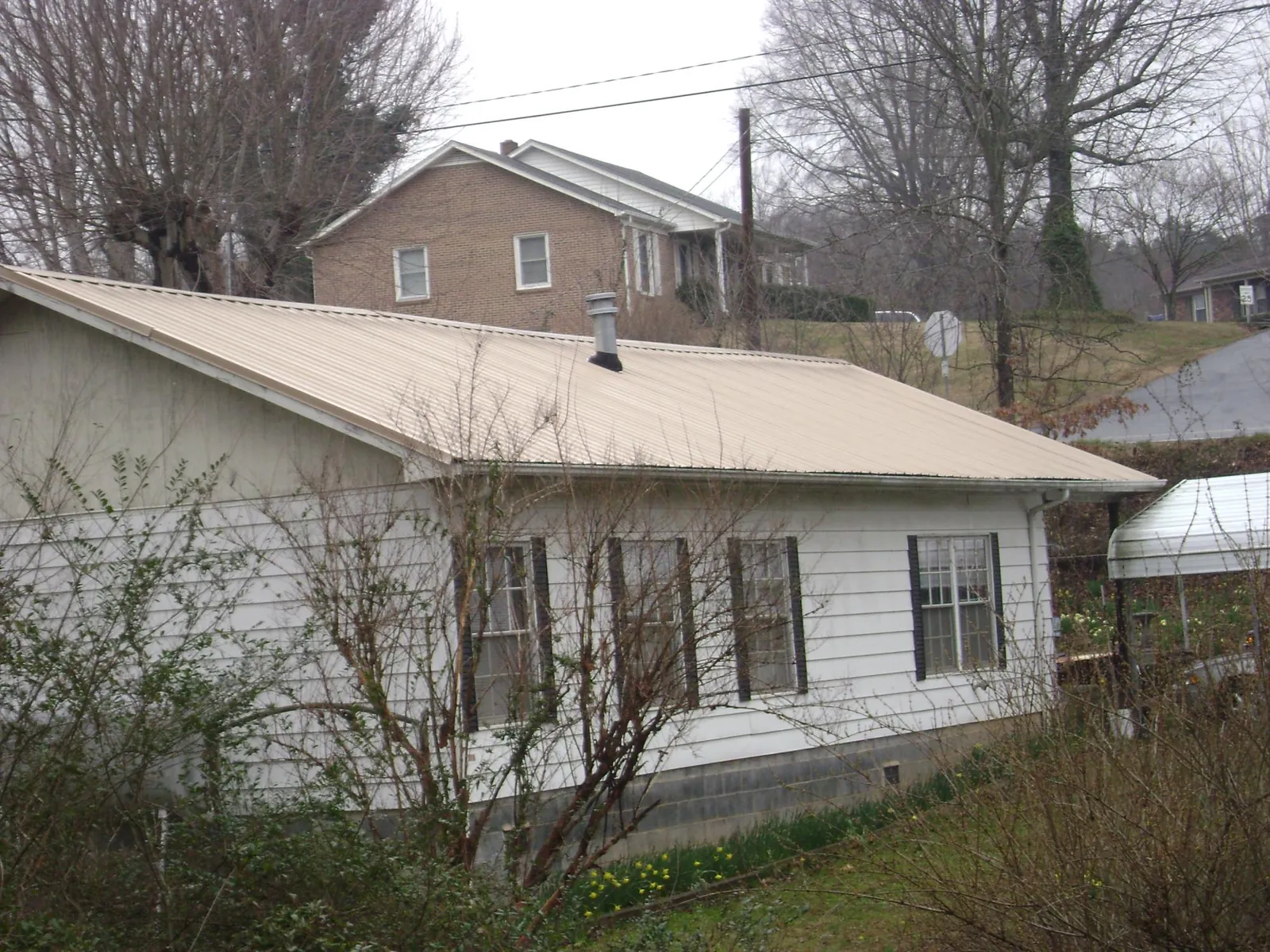 Tan metal roof on a white sided house set into a hillside — Commercial Roofing by Roofing Brothers in Kendallville