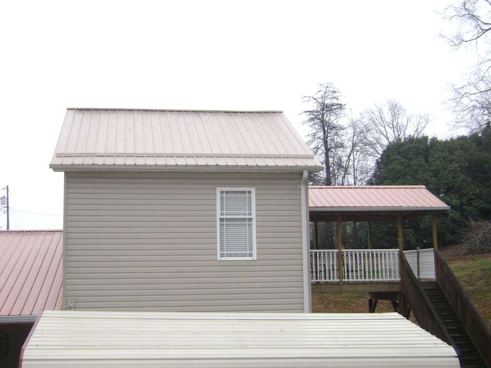 Tan metal roofs on a two story addition and attached porch, from a Roof Replacement job in Kendallville